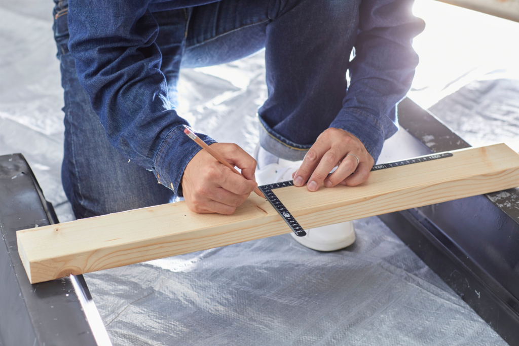 Artisan traçant une mesure sur une planche de bois avec une équerre