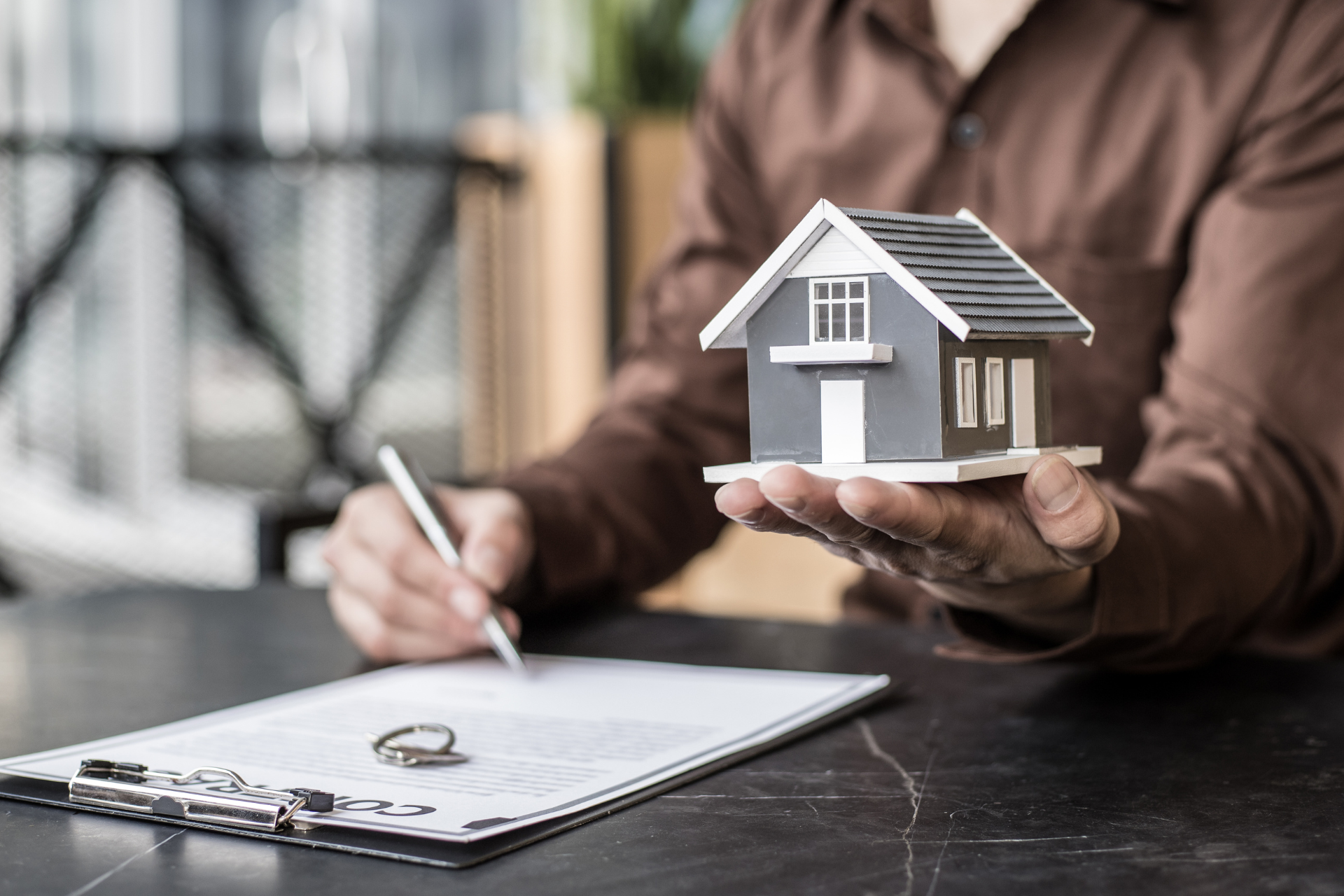 Personne tenant une maquette de maison avec un contrat et des clés sur la table
