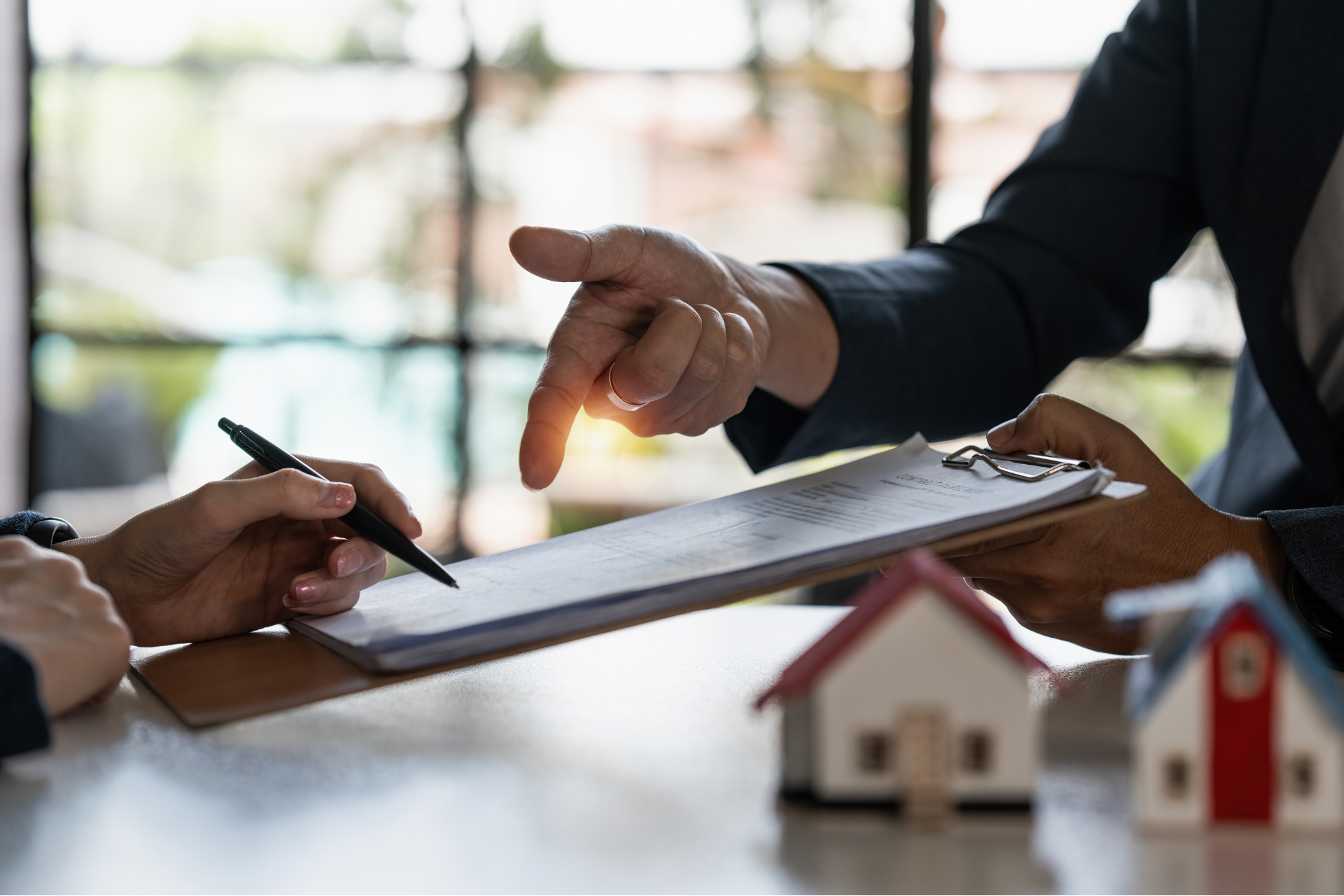 agent immobilier qui montre du doigt un papier à une femme qui a un stylo dans les mains prête à signer
